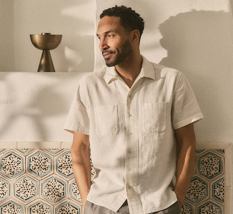 Man wearing a light-colored shirt and gray pants standing in a room with decorative tiles.